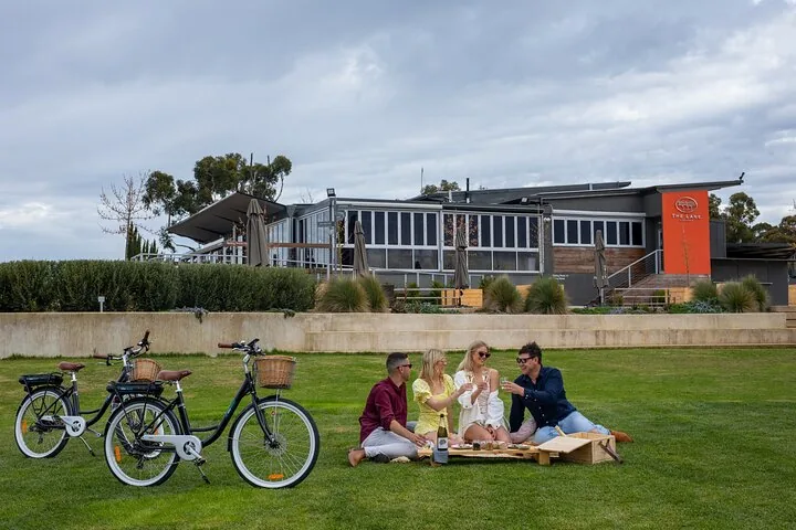 Riders relaxing on the lawn in front of a cellar door, e-bikes parked