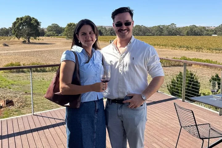 A couple with wine glasses on a deck above the vineyards