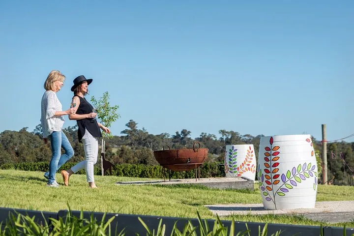 Two visitors walking past painted barrels on a cellar door lawn